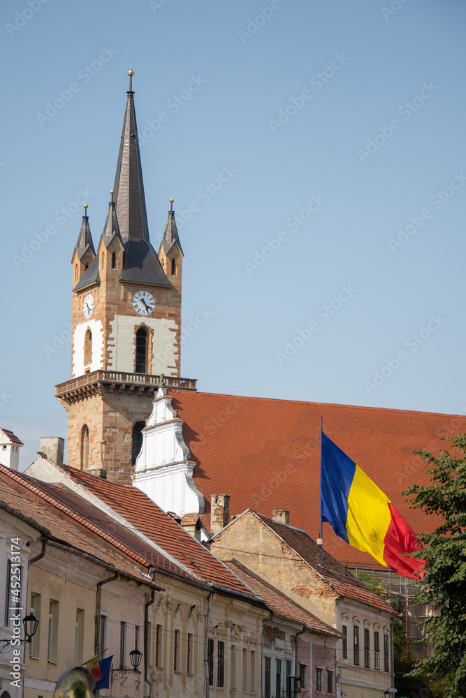  Evangelical Church Tower  in Bistrita ,august 2021,and the flag of Romania ,view from Nicolae  Titulescu street