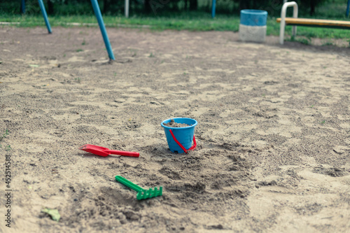 Abandoned toys on an empty playground. Bucket, shovel and rake in the sand