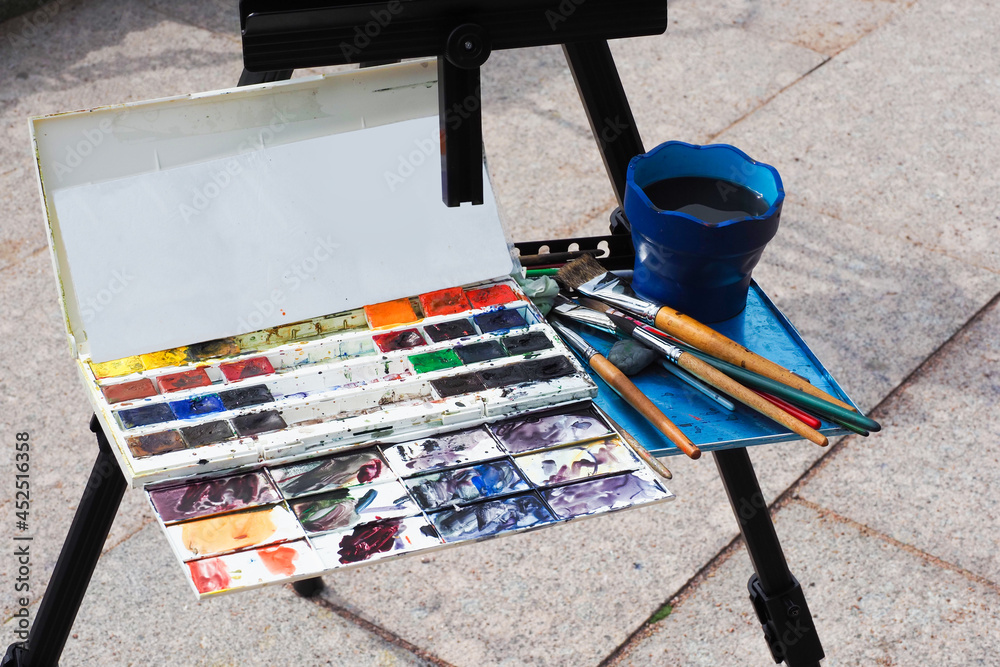 Artist painting on the street. Street artist, plein air. Brushes and paints on the easel Artist painting on the street. Street artist, plein air. Brushes and paints on the easel