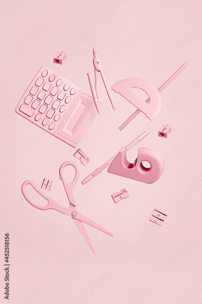 Collection of school girly equipment colored in pastel pink flying and levitate on a pastel pink background. Creative back to the school and office concept. Surreal monochrome composition.