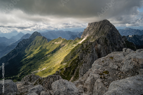 Panorama view of mountain peaks over Montasio Plateau, with Jof di Montasio partially covered by clouds, in summer.