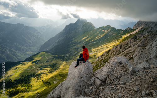Young tourist, hiker siting on the top of the hill mountains and looking at beautiful summer sunset
