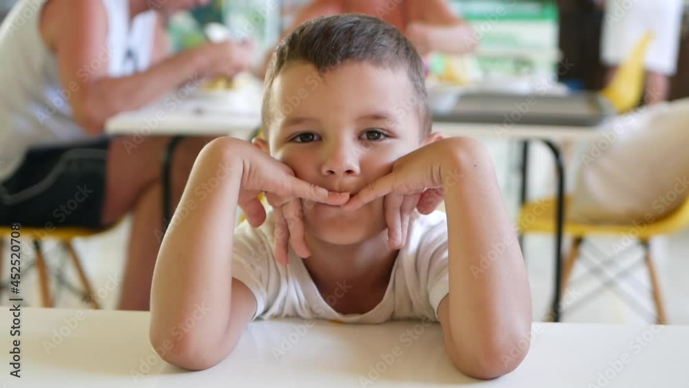 A handsome boy is sitting at a table in the dining room and is bored waiting for his lunch. Immediate children's emotions A handsome boy is sitting at a table in the dining room and is bored waiting for his lunch. Immediate children's emotions