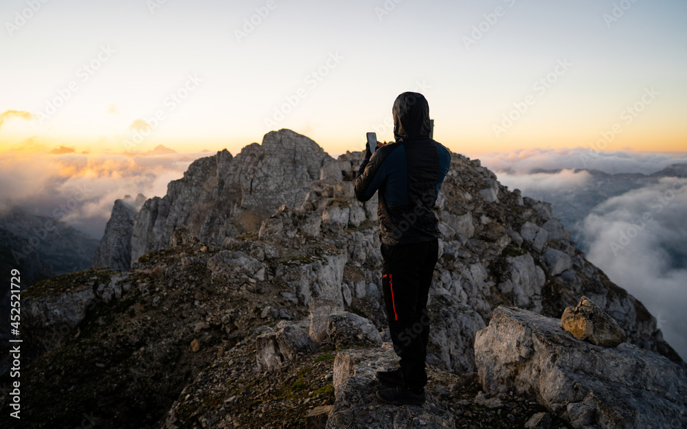 Climber ascent. Scenic landscape photo composite. Man on top of a mountain watching the colorful sunset. Traveller photographing the beautiful nature scenics with smartphone while on vacation