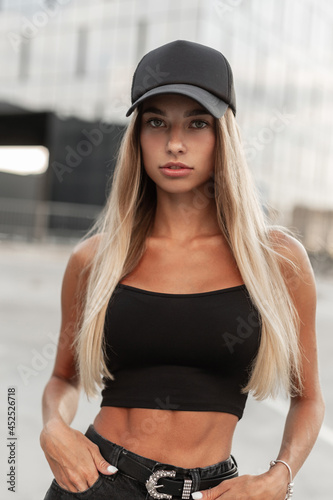 Cool beautiful woman in stylish black cap with mockup for design and fashionable black blank t-shirt on the street © alones