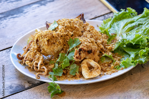 Fried squid with galic and coriander on top in white dish on wood table, ready to eat. photo
