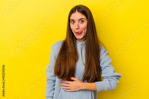 Young caucasian woman isolated on yellow background touches tummy, smiles gently, eating and satisfaction concept.