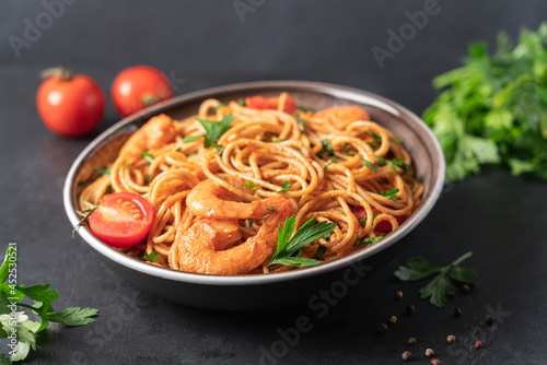 Spaghetti with shrimps in tomato cream sauce on black background