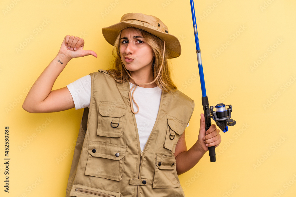 Young caucasian blonde fisherwoman holding a rod isolated on yellow background feels proud and self confident, example to follow. Young caucasian blonde fisherwoman holding a rod isolated on yellow background feels proud and self confident, example to follow.
