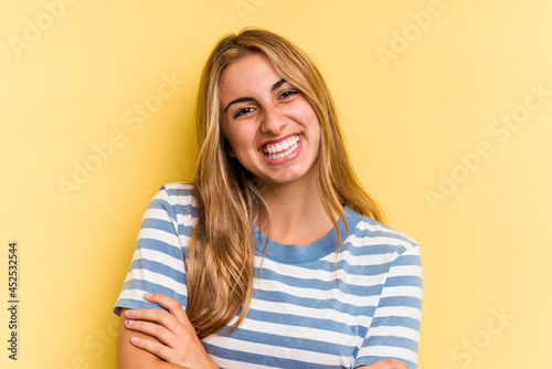 Young caucasian blonde woman isolated on yellow background  who feels confident, crossing arms with determination. © Asier