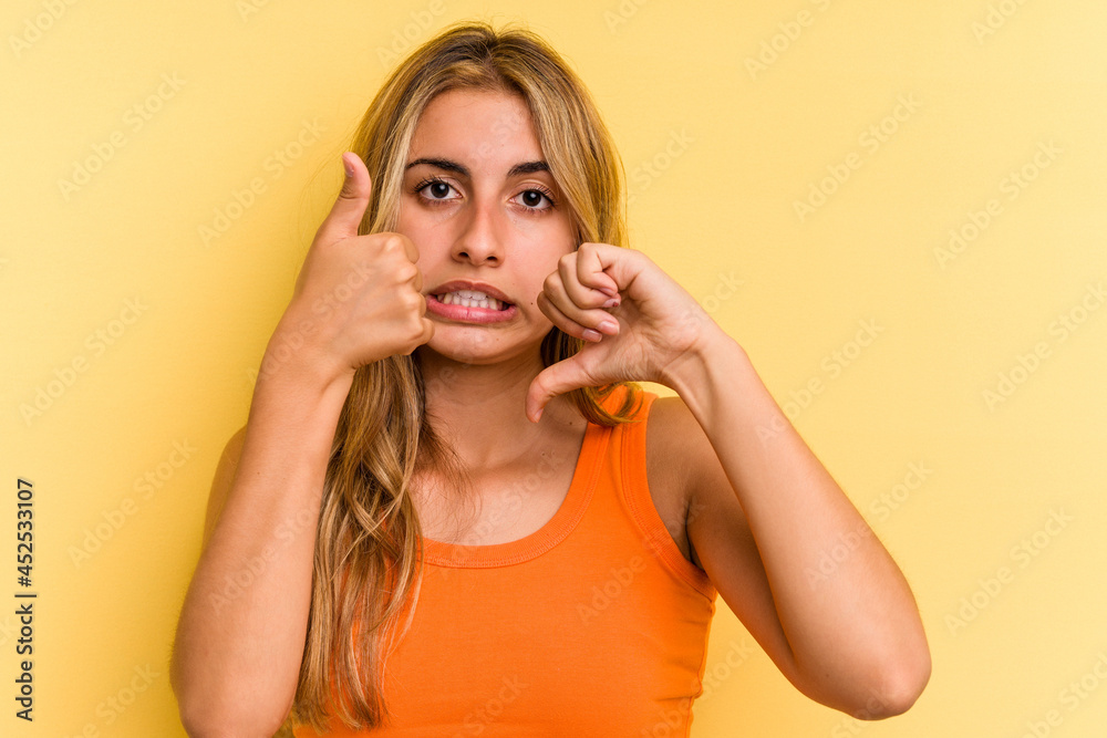 Young caucasian blonde woman isolated on yellow background showing thumbs up and thumbs down, difficult choose concept Young caucasian blonde woman isolated on yellow background showing thumbs up and thumbs down, difficult choose concept