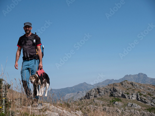 Closeup of a Caucasian man on top of the mountain in Spain hiking in the mountains with his dog on the harness and holding it with his arm