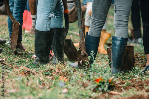 pies de personas con botas de hule y palas reunidos para sembrar plantas y reforestar