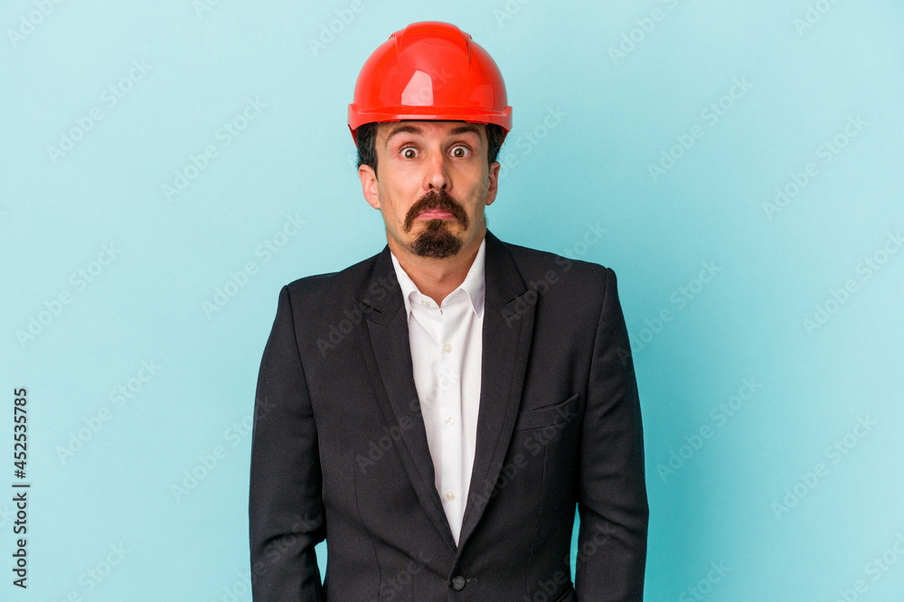 Young architect caucasian man isolated on blue background shrugs shoulders and open eyes confused. Young architect caucasian man isolated on blue background shrugs shoulders and open eyes confused.