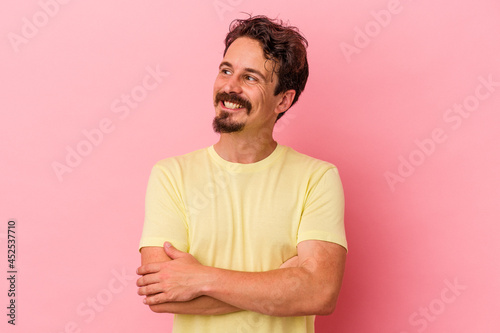 Young caucasian man isolated on pink background smiling confident with crossed arms.