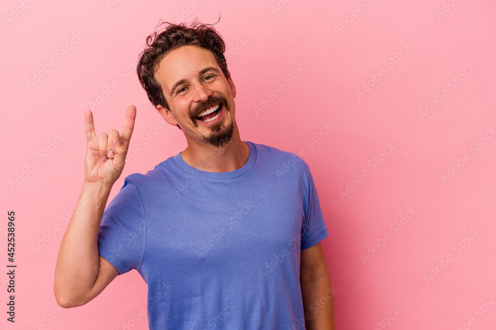 Young caucasian man isolated on pink background showing a horns gesture as a revolution concept. Young caucasian man isolated on pink background showing a horns gesture as a revolution concept.
