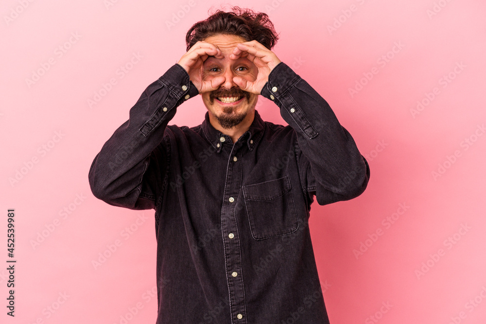 Young caucasian man isolated on pink background showing okay sign over eyes