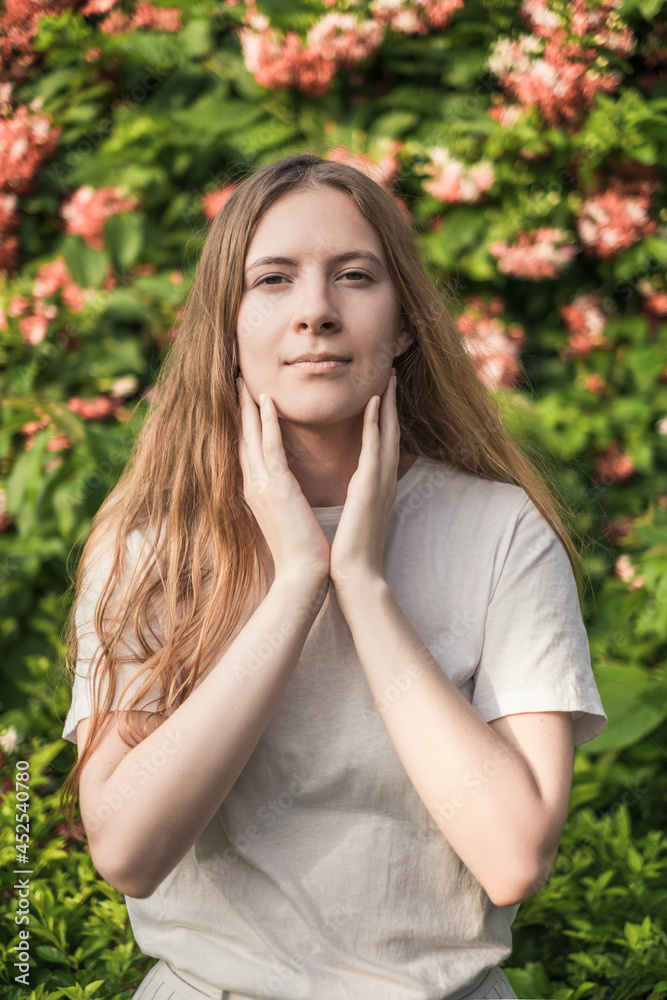 Portrait of attractive caucasian woman with long blond hair in the park. Natural beauty without make-up. Pink flowers on the background. Portrait of attractive caucasian woman with long blond hair in the park. Natural beauty without make-up. Pink flowers on the background.