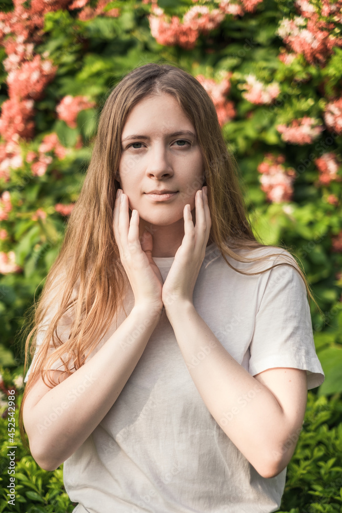 Close-up portrait of beautiful caucasian woman with long blond hair in the park. Natural beauty, make up free. Pink flowers on the background. Close-up portrait of beautiful caucasian woman with long blond hair in the park. Natural beauty, make up free. Pink flowers on the background.