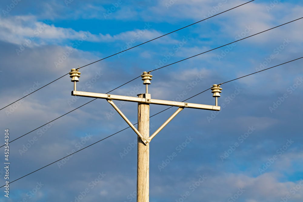 Old wooden power pole with wires on insulators against clouded sky Old wooden power pole with wires on insulators against clouded sky