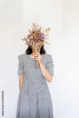 Young pretty woman in striped vintage dress holding a dried flower bouquet on white background. Florist minimal concept.