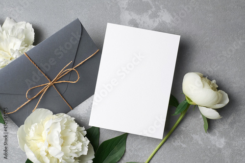 Card mockup with copy space, envelope and white peony flowers on grey