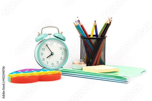 School items. Alarm clock, notebooks, pencils for drawing and silicone toy popit on  white background. Concept of education, back to school, creativity and learning. Copy space.