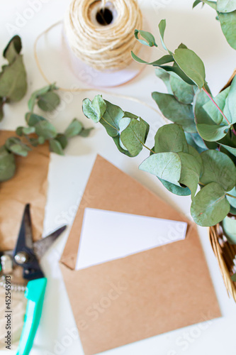 Creative retro style composition of craft envelopes, blank paper sheet and eucalyptus branches on white background. Florist, flower shop, gift concept.