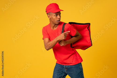 Young delivery man in red uniform running over isolated background.