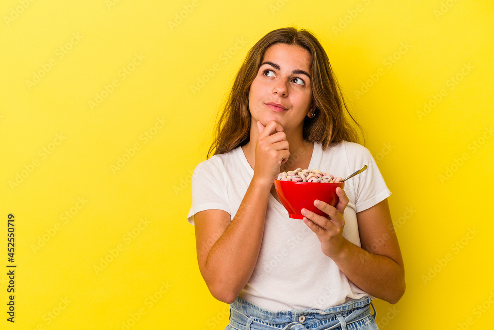 Young caucasian woman holding cereals isolated on yellow background looking sideways with doubtful and skeptical expression. Young caucasian woman holding cereals isolated on yellow background looking sideways with doubtful and skeptical expression.