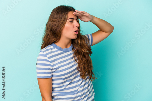 Young caucasian woman isolated on blue background looking far away keeping hand on forehead.
