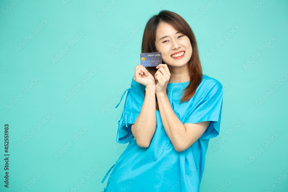 Portrait of young Asian woman in blue patient suit holding credit card isolated on green background Portrait of young Asian woman in blue patient suit holding credit card isolated on green background