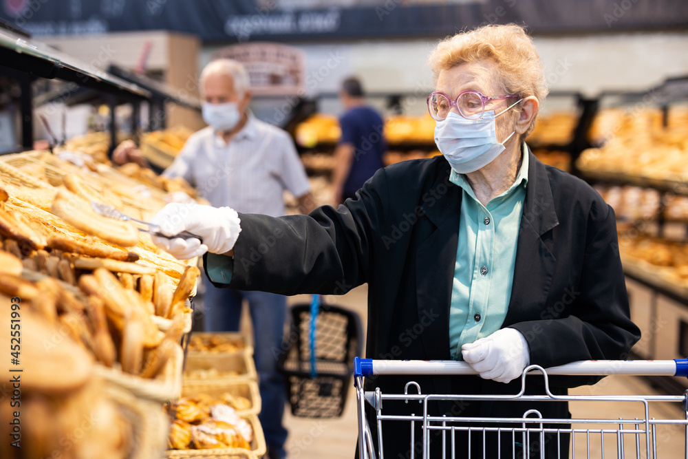 older woman with glasses chooses buns and bread in supermarket bakery