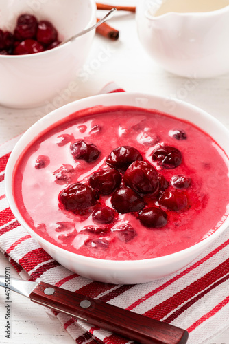 Sour cherry soup in a white bowl on a white background. Hungarian cold cherry soup with cream or sour cream, sugar and cinnamon. Sweet summer soup.