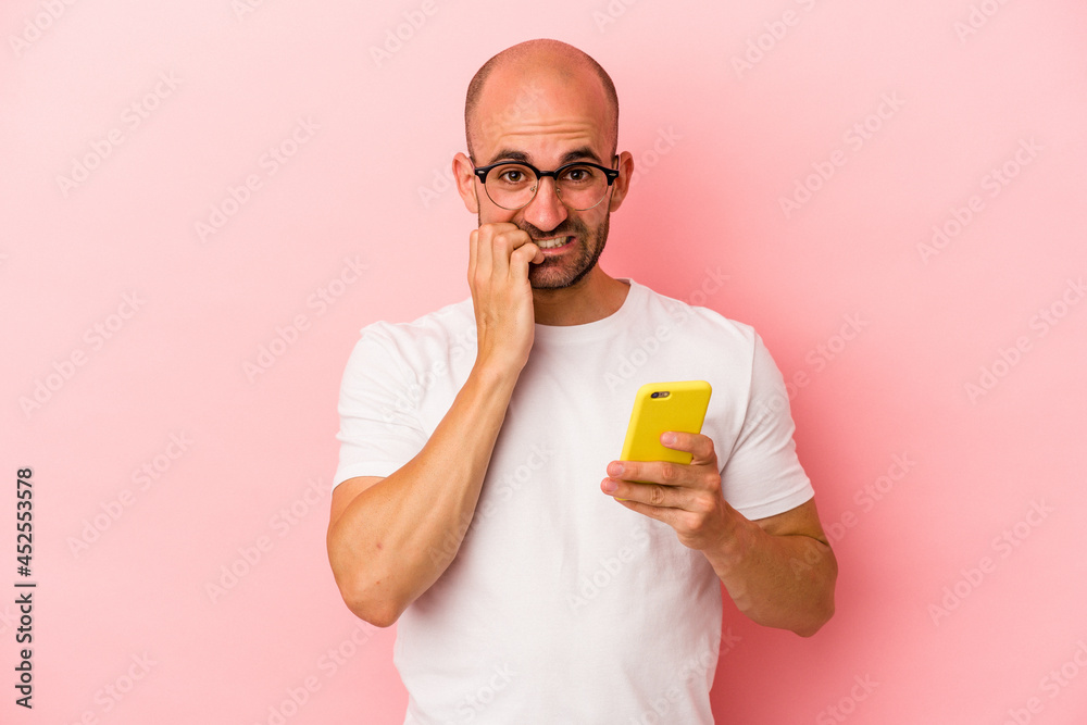 Young caucasian bald man holding mobile phone isolated on pink background biting fingernails, nervous and very anxious. Young caucasian bald man holding mobile phone isolated on pink background biting fingernails, nervous and very anxious.