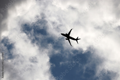Silhouette of airplane flying up in the blue sky with white and dark clouds. Passenger plane at flight, travel concept © Oleg