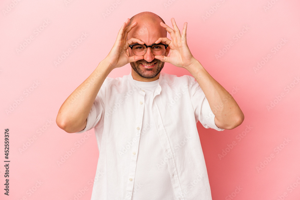 Young caucasian bald man isolated on pink background  showing okay sign over eyes