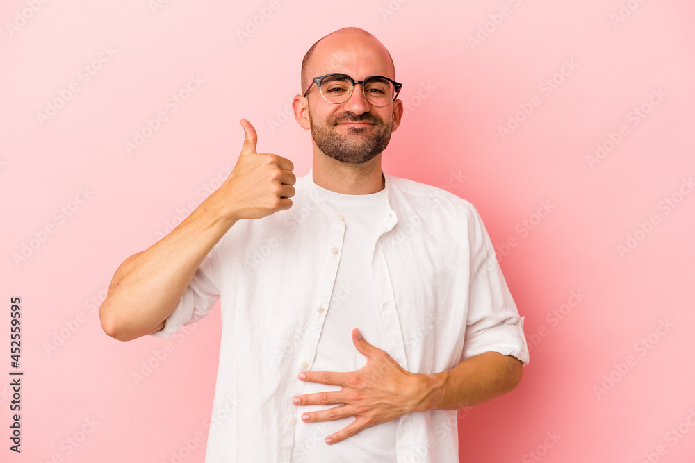 Young caucasian bald man isolated on pink background touches tummy, smiles gently, eating and satisfaction concept. Young caucasian bald man isolated on pink background touches tummy, smiles gently, eating and satisfaction concept.