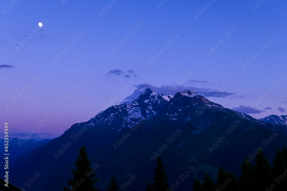 Sunrise or sunset over the mountain. Beautiful pink sky with clouds in alpine landscape and moon.