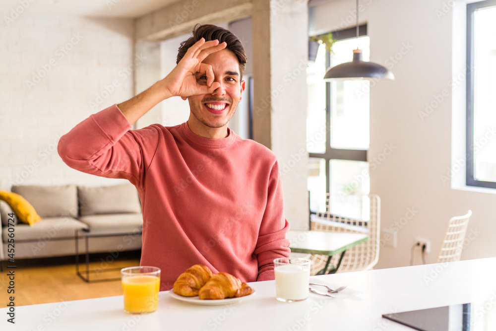Young mixed race man having breakfast in a kitchen on the morning excited keeping ok gesture on eye. Young mixed race man having breakfast in a kitchen on the morning excited keeping ok gesture on eye.