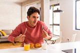 Young mixed race man eating croissant in a kitchen on the morning