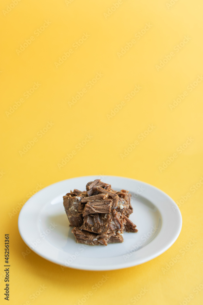 Canned beef stew on white plate with parsley leaf, yellow background