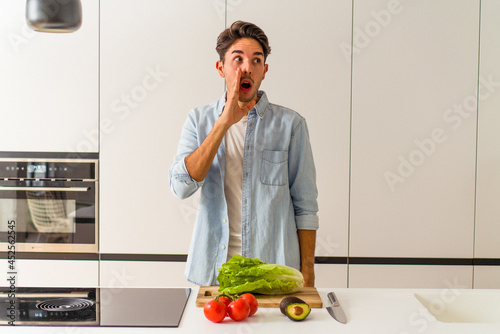Young mixed race man preparing a salad for lunch is saying a secret hot braking news and looking aside