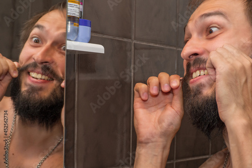 A bearded man twists his mustache in front of the bathroom mirror