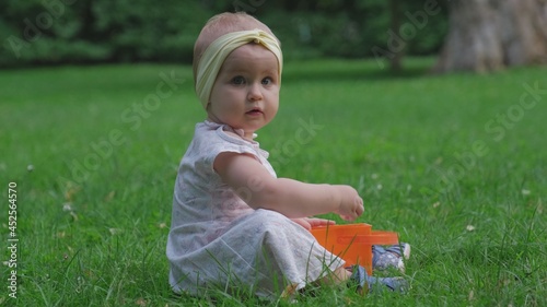 Cute Adorable Baby Infant Toddler Girl Playing on Vivid Green Grass Lawn in City Park 