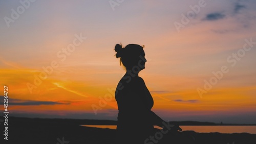 Silhouette of Young Woman Sitting Meditating and Exercising Yoga Lotus Position on Seaside Beach during Evening Sunset	