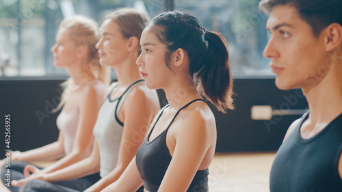 Young diversity sporty people practicing yoga lesson with instructor. Multi racial group of women and man exercising healthy lifestyle in fitness studio. Sport activity, gymnastics or dancing class.