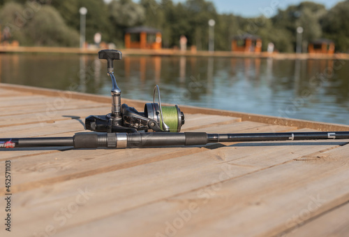 Fishing rod or angler closeup on wood coast over river or lake in summer.