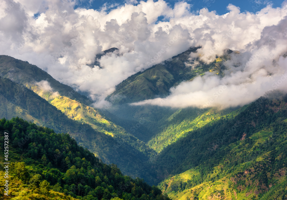 Mountains in low clouds at sunny day in summer. Nepal. Aerial view of mountain hills with green trees. Beautiful landscape. Top view of himalayan mountains with forest. Nature. Woods in spring