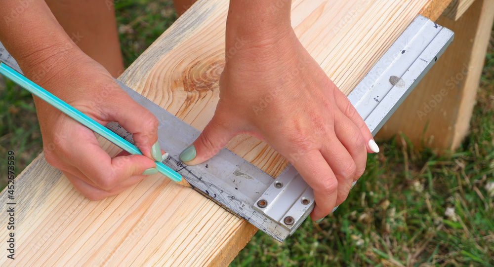 Woman carpenter makes pencil markings on a wooden board. DIY in the backyard. Woman carpenter makes pencil markings on a wooden board. DIY in the backyard.